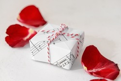 Gift box made of music notes and rose petals on light background