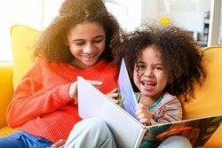 Cute African-American sisters reading book at home
