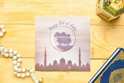 Greeting card for Eid al-Adha (Feast of the Sacrifice) with Quran, lamp and tasbih on wooden background