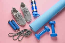 Sport shoes, yoga mat, bottle of water, dumbbells and skipping rope on color background
