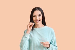 Beautiful young woman taking pills on color background