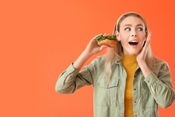 Surprised young woman with tasty vegan burger on color background