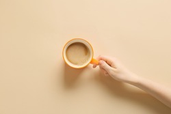 Female hand with cup of coffee on yellow background