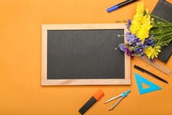 Blank chalkboard, flowers and stationery on color background