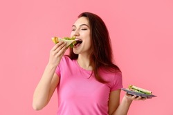Young woman eating tasty sandwich on color background
