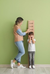 Woman measuring height of her little son near color wall