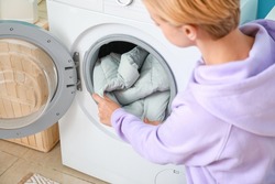 Young woman taking down jacket from washing machine in bathroom