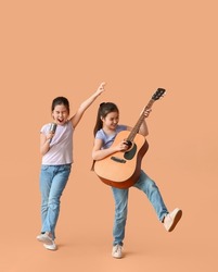 Funny little sisters with guitar and microphone on color background