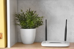 Modern wi-fi router and houseplant on shelf near light wall