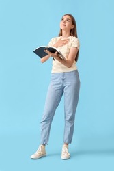 Pretty young woman reading Holy Bible on blue background