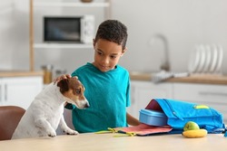 Cute little boy with funny dog putting his school lunch in bag