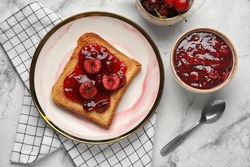 Plate with toast and sweet cherry jam on light background