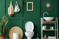 Interior of restroom with toilet bowl, sink and green wall