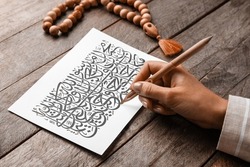 Arabic calligraphist writing on paper sheet against wooden background