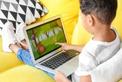 Little African-American boy pointing at laptop while watching cartoons on sofa at home