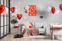 Interior of room decorated for Valentine's day with air balloons and comfortable sofas near grey brick wall
