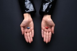 Hands with blue and red pills on dark background. Concept of choice