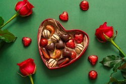 Heart shaped box with tasty chocolate candies and roses on green background
