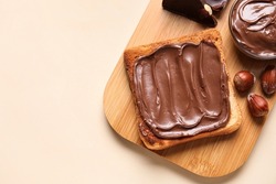 Board of bread with chocolate paste and hazelnuts on beige background, closeup