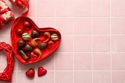 Heart shaped box with tasty chocolate candies on tile background
