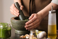 Woman making pesto sauce with mortar and pestle on table in kitchen