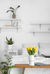 Vase with tulips and laptop on bench in bedroom