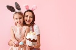 Little girl, her mother with tasty Easter cake and eggs on pink background