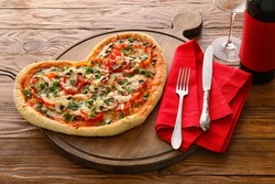 Board with tasty heart-shaped pizza on wooden background. Valentine's Day celebration