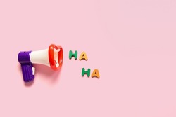 Composition with megaphone and text HA HA for April Fools Day celebration on pink background