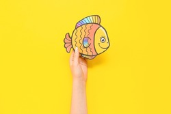 Female hand with paper fish on yellow background. April Fools Day celebration