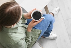 Young woman with cup of hot coffee in kitchen, closeup