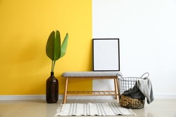 Modern bench with frame, palm leaves in vase and basket near color wall