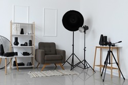 Interior of light photo studio with armchair, shelf unit and different modern equipment