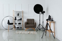 Interior of photo studio with armchair, shelf unit and different modern equipment near light wall