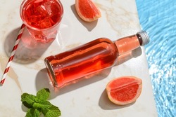 Bottle and glass of fresh grapefruit soda near swimming pool