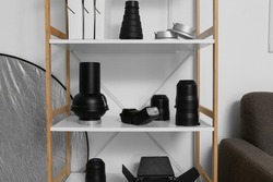 Shelf unit with different modern equipment for photo studio near light wall