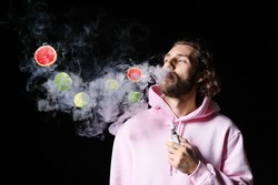 Young man smoking electronic cigarette with fruit flavor on black background