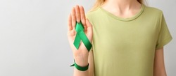 Woman holding green ribbon on light background with space for text, closeup. Liver cancer concept