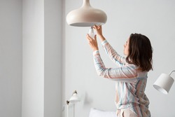 Woman changing light bulb in hanging lamp at home