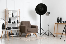 Interior of light photo studio with armchair, shelf unit and different modern equipment
