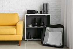 Armchair and shelf unit with different equipment near white brick wall in photo studio