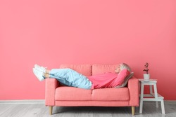 Mature woman relaxing on sofa near pink wall