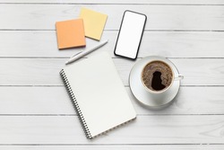 Composition with cup of coffee, notebook, sticky notes and mobile phone on white wooden background