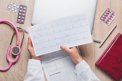 Female doctor with cardiogram, pills and stethoscope on wooden background