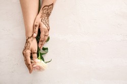 Female hands with beautiful henna tattoo and rose flower on light background, closeup