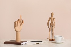 Wooden hand, notebooks, mannequin and cup of coffee on table against beige background