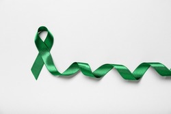 Green ribbon on light background, top view. Liver cancer concept