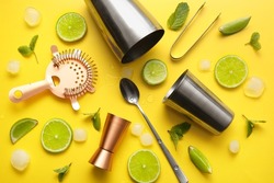 Different bartender tools and cocktail ingredients on yellow background, closeup