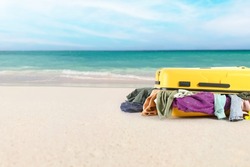 Suitcase with heap of clothes on sea beach. Travel concept