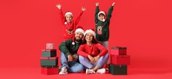 Happy family in Santa hats and with Christmas gifts on red background